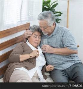 Asian Senior Woman taking medicines and drinking water while sitting on couch. Old man take care his wife while her illness at the house.
