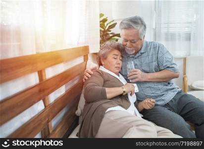Asian Senior Woman taking medicines and drinking water while sitting on couch. Old man take care his wife while her illness at the house.healthcare and medicine concept.