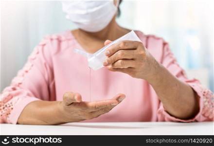 Asian Senior Woman wear surgical mask in pink shirt pouring hand sanitizer portable gel on her palms and hands for prevent and protection coronavirus or Covid-19. Pandemic, Antiseptic, Hygiene and Healthy and Health care
