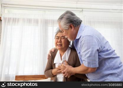 Asian senior woman with pain on heart on sofa in living room and take care by her husband, Health problem and feeling sick