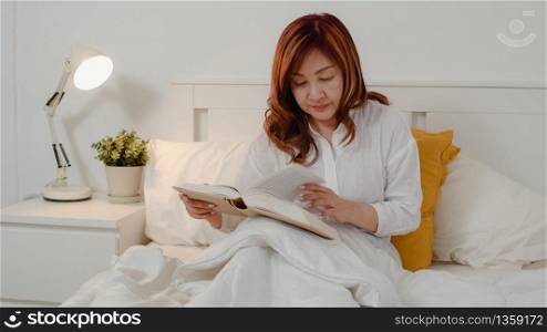 Asian senior women relax at home. Asian Senior Chinese female enjoy rest time read book while lying on bed in bedroom at home at night concept.