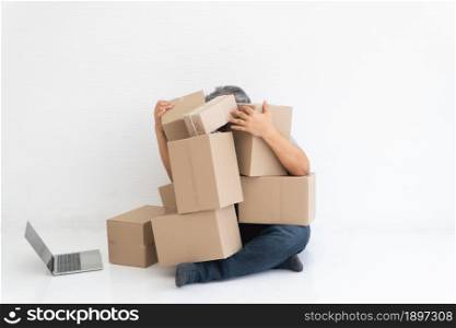 Asian Shopaholic sitting on the floor in the living room and Cardboard Box on top of him after The courier delivered to the home. Concept of shopping online and Shopaholic.