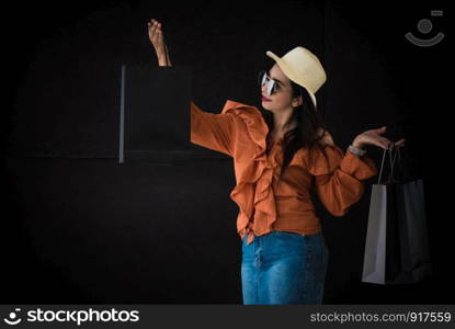 Asian shopping woman enjoy with Black Friday shopping bag on black background. Shopaholics and beauty fashion theme.