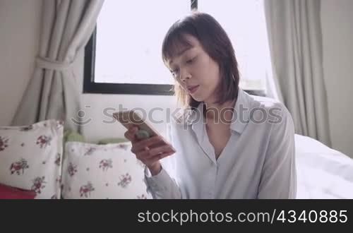Asian short hair woman holding smartphone with reading on online information at living room, internet knowledges accessibility, worldwide data, distant communication, relaxing weekend activity at home