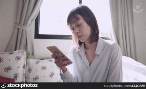 Asian short hair woman holding smartphone with reading on online information at living room, internet knowledges accessibility, worldwide data, distant communication, relaxing weekend activity at home