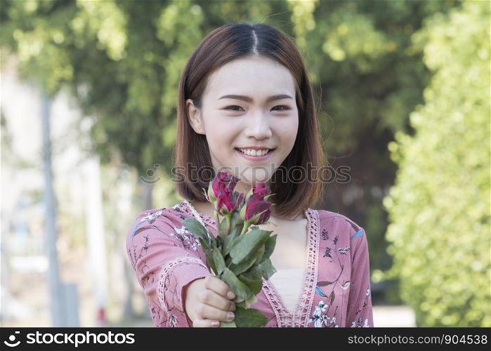 Asian smiling girl holding red roses in park