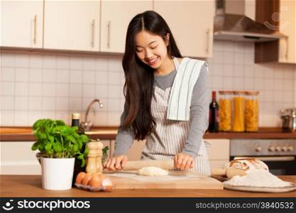 Asian smiling woman is baking bread in her home kitchen