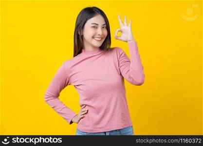 Asian smiling young woman gesturing ok sign for approval or agreement on isolated yellow color background, wearing winter cozy sweater indoors studio,happiness and optimistic decision copy space