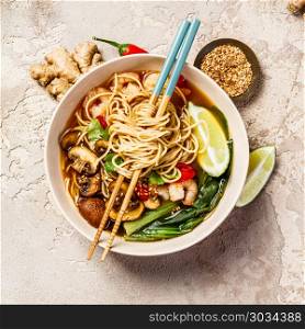 Asian soup with noodles (ramen), with miso paste, soy sauce, greens, mushrooms and shrimps prawn. On a stone table, with chopsticks, ginger and lime. Asian soup with noodles. Asian soup with noodles