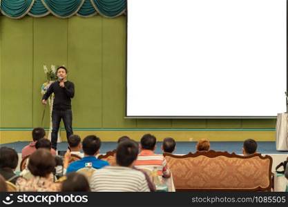 Asian Speaker with casual suit on the stage present the screen in the conference hall or seminar meeting, business and education concept