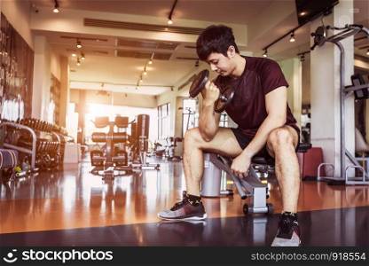 Asian sport man lifting dumbbell at fitness bench with gym equipment background. Sport exercise and People lifestyles concept.