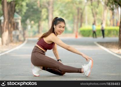 Asian sport woman sit and do right leg stretching also look at camera after exercise in park or garden in the morning.