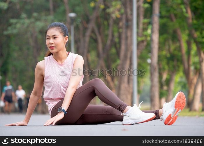 Asian sport woman sit and stretching body and leg on road of park or garden in the morning.
