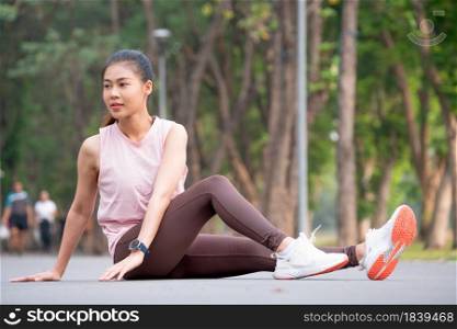 Asian sport woman sit and stretching body and leg on road of park or garden in the morning.