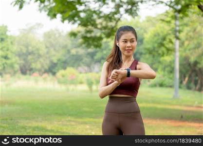 Asian sport woman touch her watch and look to left side during exercise in park or garden with morning light.
