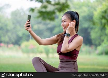 Asian sport woman use mobile phone to selfie during sit in park after exercise in the morning.