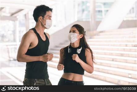 Asian sportive man and woman wearing face mask to protect virus and doing exercise by running or jogging outdoor in the morning. Health and Sport Concept.