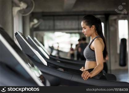 Asian sporty woman walk cardio on treadmills to warm up before running exercise in fitness gym with copy space for text. Bodybuilding and healthy lifestyle concept.
