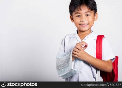 Asian student kid boy wearing student thai uniform accident broken bone wearing splint arm plaster fiberglass cast covering arm in cast at studio shot isolated on white background, back to school