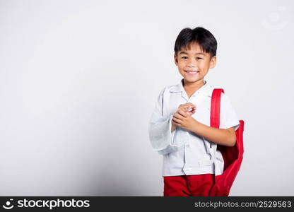 Asian student kid boy wearing student thai uniform accident broken bone wearing splint arm plaster fiberglass cast covering arm in cast at studio shot isolated on white background, back to school