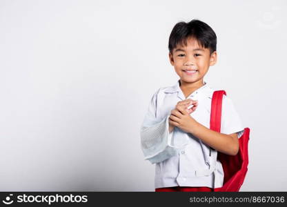 Asian student kid boy wearing student thai uniform accident broken bone wearing splint arm plaster fiberglass cast covering arm in cast at studio shot isolated on white background, back to school