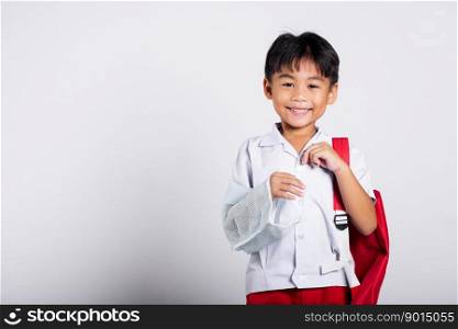 Asian student kid boy wearing student thai uniform accident broken bone wearing splint arm plaster fiberglass cast covering arm in cast at studio shot isolated on white background, back to school