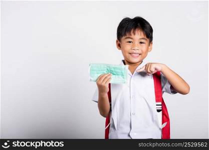 Asian student kid boy wearing student thai uniform and pointing finger to protect mask before to go to school in studio shot isolated on white background, preschool, new normal back to school