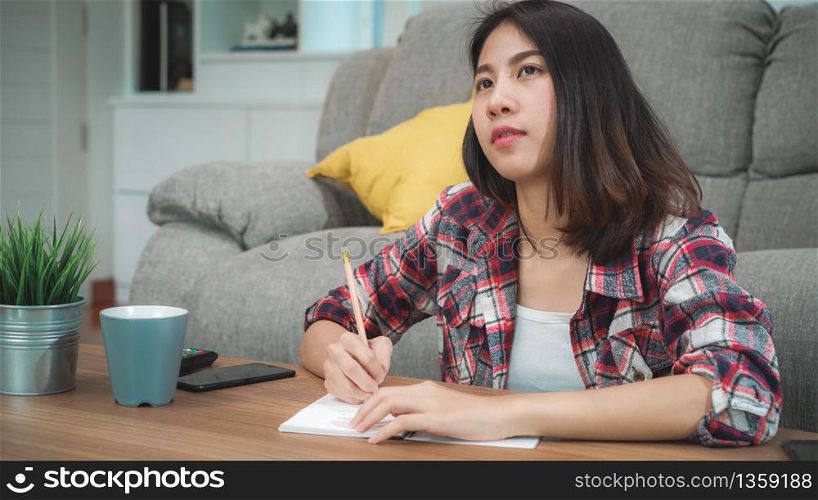Asian student woman do homework at home, female using tablet for searching on sofa in living room at home. Lifestyle women relax at home concept.