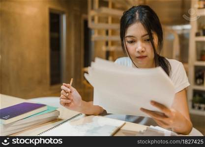 Asian student women reading books in library at university. Young undergraduate girl do homework, read textbook, study hard for knowledge on lecture desk at college campus overtime night.