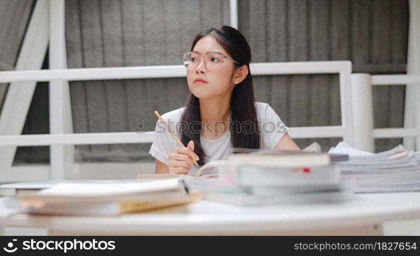 Asian student women reading books in library at university. Young undergraduate girl do homework, read textbook, study hard for knowledge and education on lecture desk at college campus.