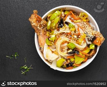 Asian style noodles with vegetables, chicken and teriyaki sauce. Top view, bowl with noodles located on a black stone background. Lunch, noodles with chicken, vegetables, spices and micro-greens. Asian style noodles with vegetables, chicken and teriyaki sauce.