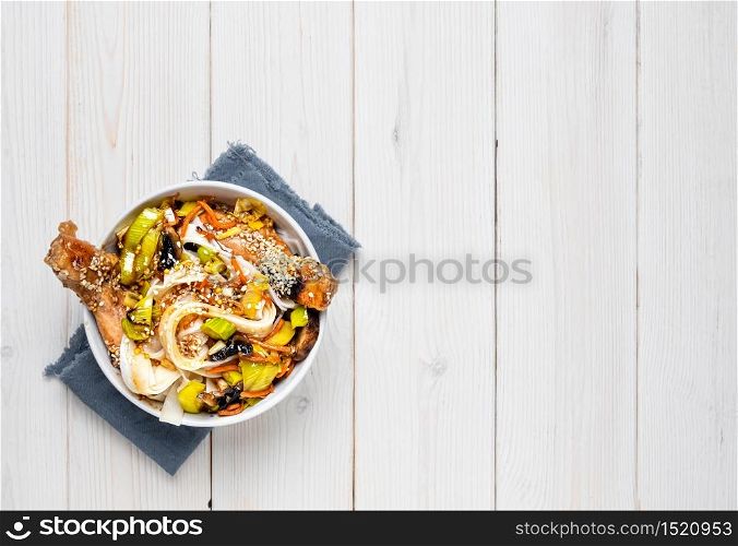 Asian style noodles with vegetables, chicken and teriyaki sauce. Top view, noodle bowl on a white wooden background with copy space. Lunch, noodles with chicken, vegetables, spices and micro-greens. Asian style noodles with vegetables, chicken and teriyaki sauce.