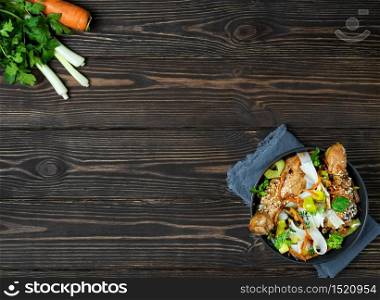 Asian style noodles with vegetables, chicken and teriyaki sauce. Layout, noodle bowl on dark wooden background with copy space. Lunch, noodles with chicken, vegetables, spices and microgreens. Asian style noodles with vegetables, chicken and teriyaki sauce.