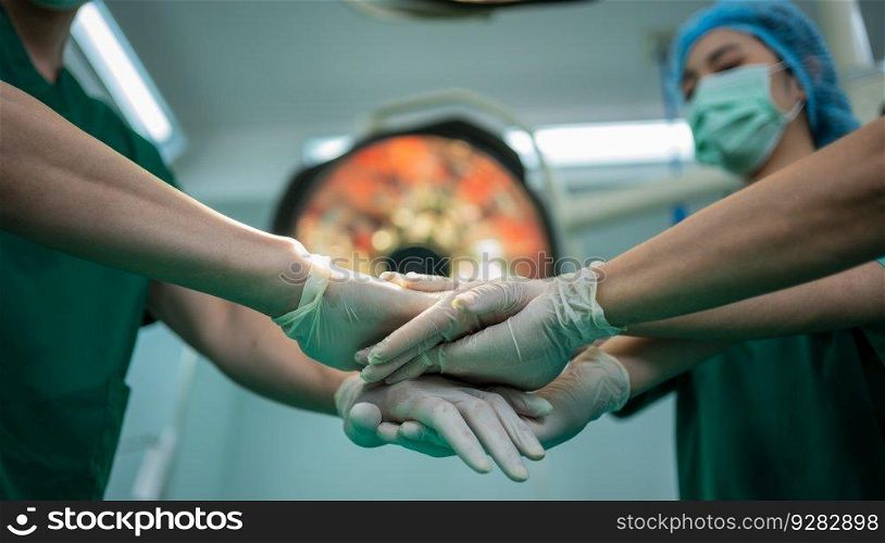 Asian surgeon and nurse with medical mask standing and join hand in operation theater at a hospital. Team of Professional surgeons. Healthcare, emergency medical service concept