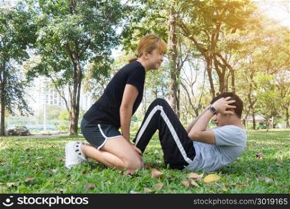 Asian sweet couple exercising together with smile on their faces on soft grass encircle with nature and warm light from the sun in the afternoon. Couple smile happily to each other. Outdoor exercise.