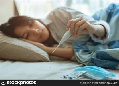 Asian teen infected with Covid-19 flu sick lying in bed due to a Corona virus pandemic, anxiously measuring check body temperature with digital thermometer.