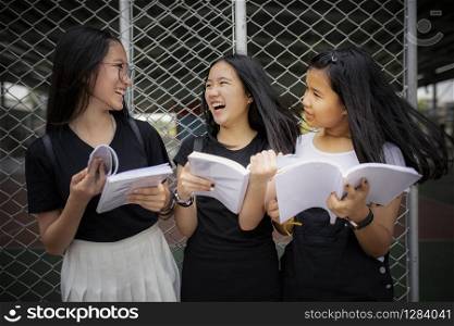 asian teenager holding school book and laughing with happiness emotion standing outdoor