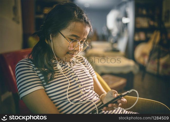 asian teenager lissening music from ear speaker phone in home living room