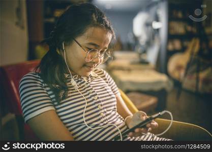 asian teenager lissening music from ear speaker phone in home living room
