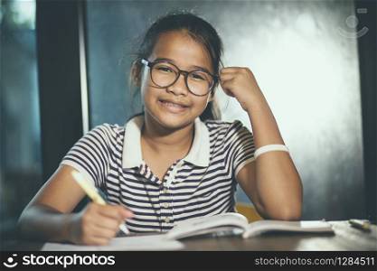 asian teenager wearing eye glasses doing home work with stack of school book foreground
