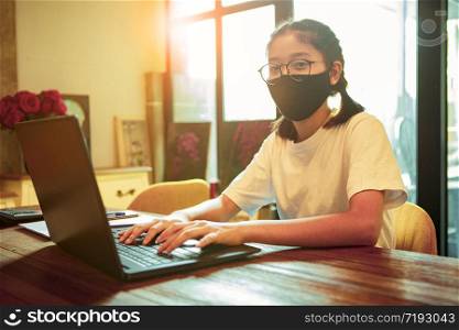 asian teenager wearing protection mask typing on computer laptop ,work from home