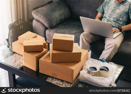 Asian teenager working in home office going over inventory and shipping on desk.