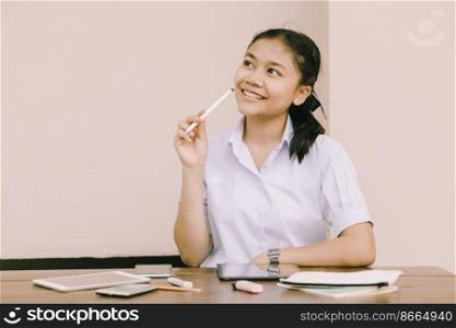 Asian Thai cute girl teen student school uniform happy smile thinking using Tablet PC for E-Learning self isolated education happy smile concept