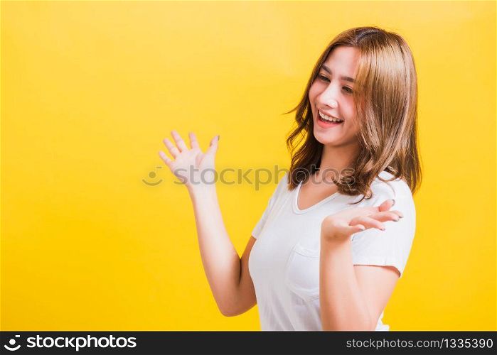 Asian Thai happy portrait beautiful cute young woman standing wear t-shirt her winning and surprised excited screaming open mouth showing hands, studio shot isolated yellow background with copy space