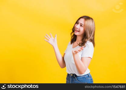 Asian Thai happy portrait beautiful cute young woman standing wear t-shirt her winning and surprised excited screaming open mouth showing hands, studio shot isolated yellow background with copy space