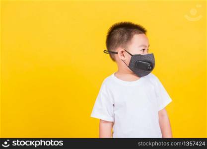 Asian Thai happy portrait cute little cheerful child boy wearing mask protective for covid-19 or pm2.5 dust he looking to side space, studio shot isolated on yellow background with copy space