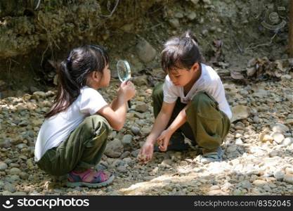 Asian tourist family, two sisters studying rocks with a magnifying glass as they travel to Pha Chor is high soil canyon cliffs at Mae Wang National parks in Chiang Mai,Thailand.