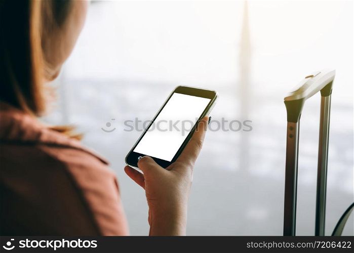 Asian tourist woman hands holding and using smartphone with blank screen waiting for flight in airport lounge.