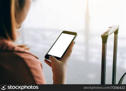 Asian tourist woman hands holding and using smartphone with blank screen waiting for flight in airport lounge.