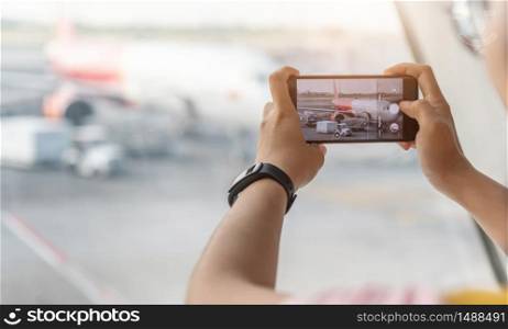 Asian traveler is Enjoying taking airplane pictures with her smartphone at the airport.